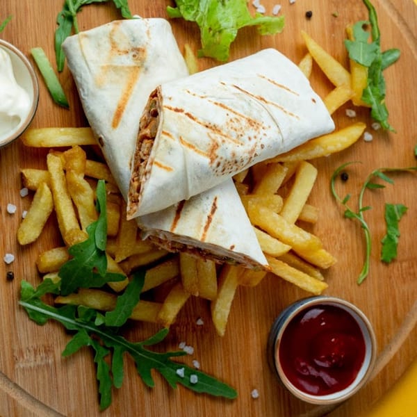 Two Rapids Chicken wraps with fries, ketchup, and mayonnaise on a wooden board.