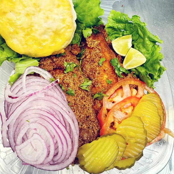 Rapids Chicken fried fish with lettuce, red onion, tomatoes, pickles, lime, and a biscuit.
