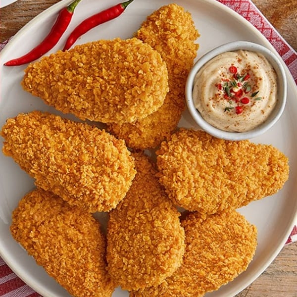 Crispy fried chicken tenders on a white plate with a side of dipping sauce and red chilies.