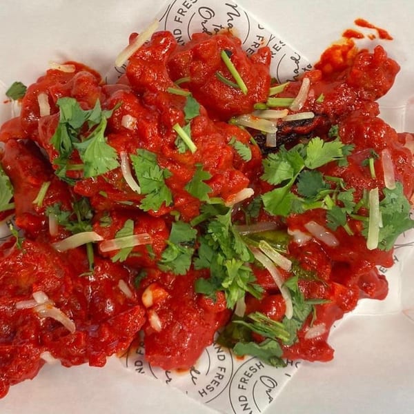 Rapids Chicken's bright red fried chicken pieces, garnished with fresh cilantro and sliced onions.