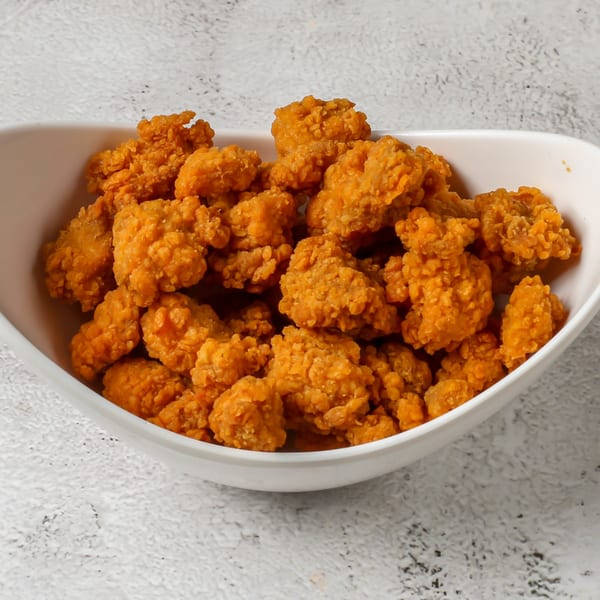 A white bowl filled with golden-brown, crispy fried chicken popcorn from Rapids Chicken.